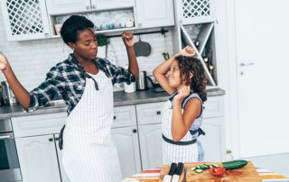 Mother and daughter dancing while cooking in the kitchen. Mother is Black, daughter is mixed race.