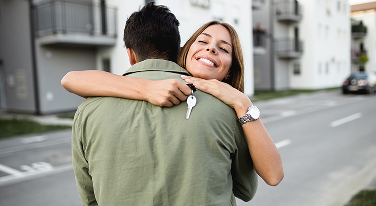 Happy young couple embracing. Young woman facing the camera over her partner's shoulder with the keys in her hand in front of their new home.