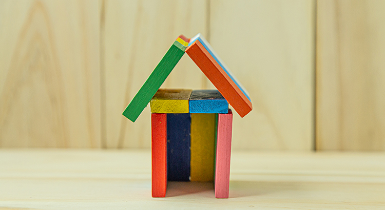 small toy house structure made from colourful pieces of wood. It is placed on a blank wooden surface