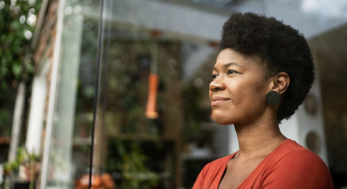 Black woman with short cropped hair looking off into the distance while standing in front of a building