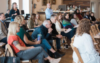 A group of real estate professionals seated in rows of chairs attentively watching a speaker present at the front of the room during a continuing education class